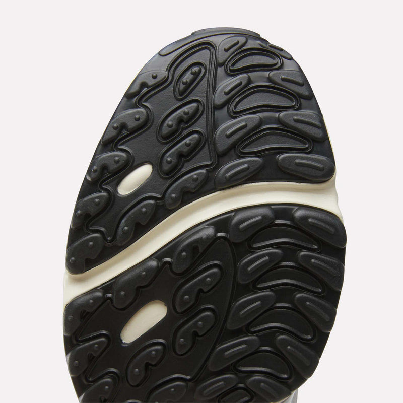 Close-up of a Men’s Daytona DMX Shoes by Reebok, highlighting the black rubber sole with a wavy, textured tread pattern featuring oval-shaped grooves and subtle air cushioning details, all set against a white background.