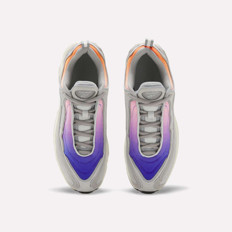 A pair of Reebok Men’s Daytona DMX Shoes in gray, showcasing gradient panels that transition from pink to purple to blue and equipped with air cushioning for superior comfort, seen from above against a white background.