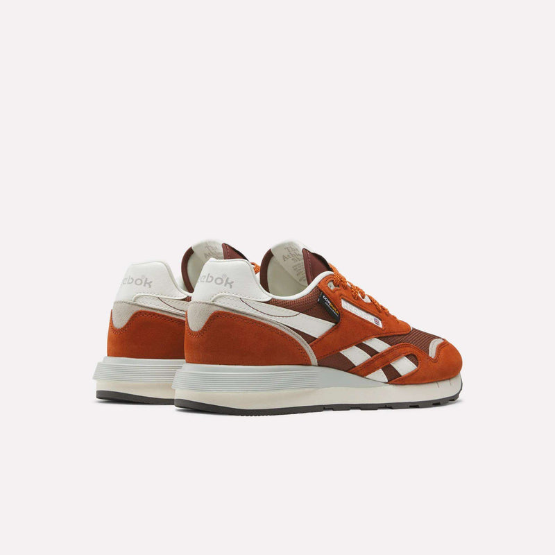 A pair of Reebok Men’s Classic Nylon 89 Shoes in orange and white, crafted from mixed materials with suede and leather accents, showcasing an EVA midsole, displayed from the back and side against a plain white background.
