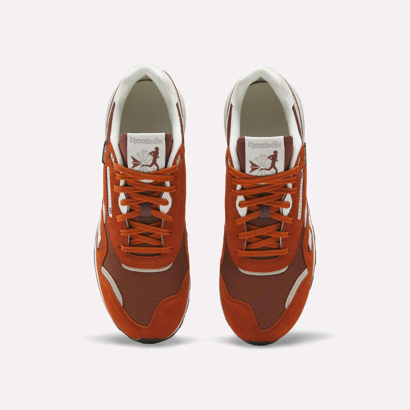A pair of Men’s Classic Nylon 89 Shoes by Reebok in red and white, viewed from above, displays the laces, mesh detailing, and branded logo on the tongue. These sneakers combine mixed materials and feature an EVA midsole for lightweight cushioning, all set against a plain white background.