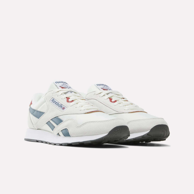 A pair of Men’s Classic Nylon Shoes from Reebok in white with blue and red accents, featuring the iconic Reebok logo on the side and tongue, displayed against a plain white background. These mixed-material sneakers are equipped with an EVA midsole for lightweight comfort and timeless style.