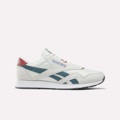 A pair of Reebok Men’s Classic Nylon Shoes in Chalk/Heritagered/Midnighttide is displayed in a side profile view against a plain white background. These mixed material sneakers showcase teal and red accents, blue side stripes, a white sole, and feature an EVA midsole for enhanced comfort.