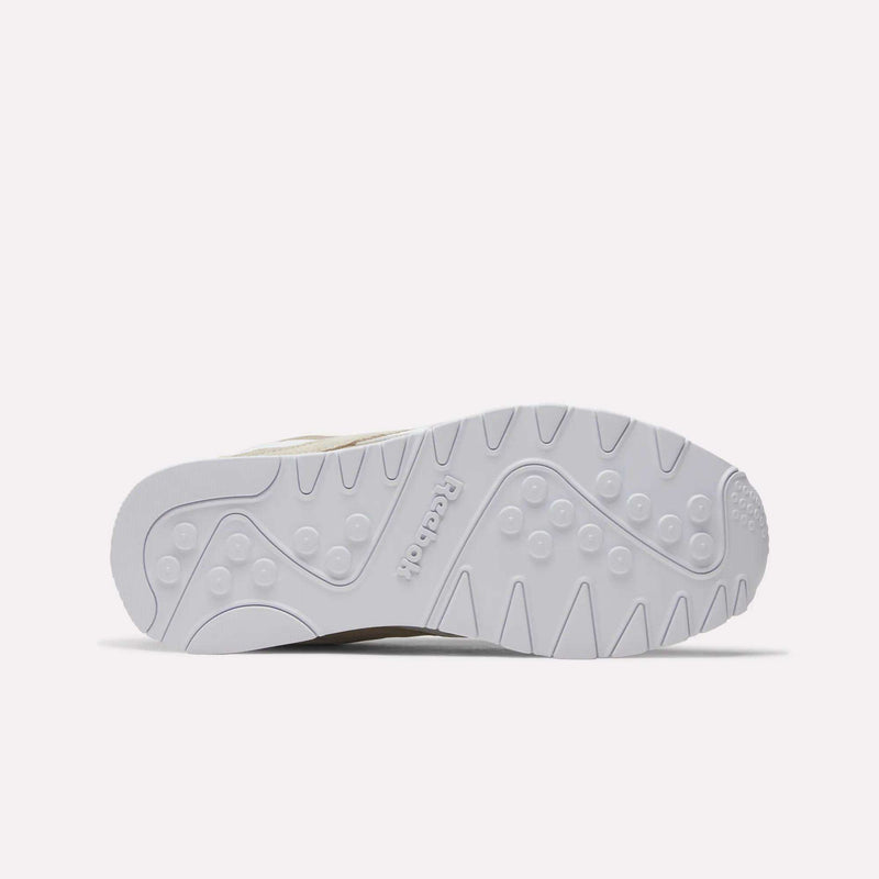 The image displays the white outsole of the Reebok Men’s Classic Nylon Shoes, showcasing an array of patterns such as zigzag lines, circular shapes, and the Reebok logo embossed at the center. Ideal for retro sneaker enthusiasts, these shoes are photographed against a simple, light-colored background.
