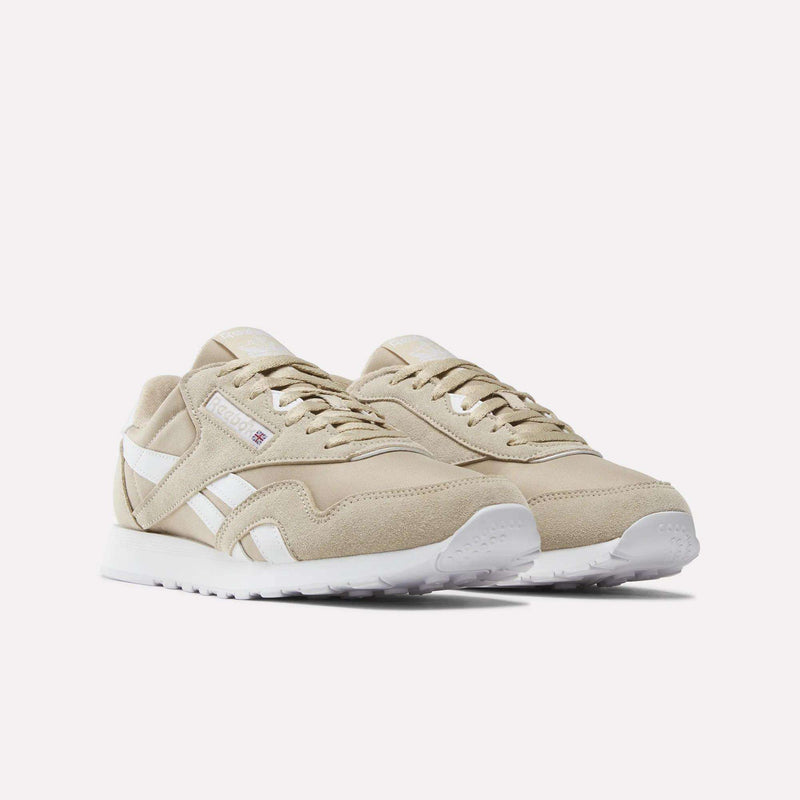 A pair of Men’s Classic Nylon Shoes by Reebok in beige, featuring white side stripes and white soles, displayed on a plain white background. These sneakers blend retro design with contemporary comfort.