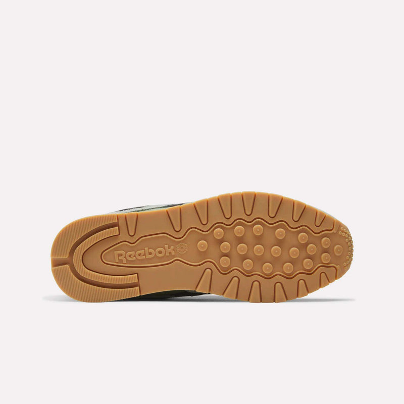 Bottom view of the Reebok Men’s Classic Leather Shoes with a tan rubber sole featuring textured tread patterns, circular grips, and the Reebok logo near the heel—highlighting the comfort of an EVA midsole—all set against a plain light background.