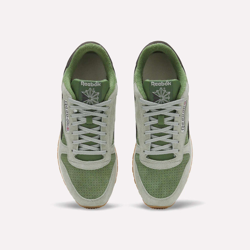 A pair of Men’s Classic Leather Shoes by Reebok in green and gray are shown from above, featuring white laces, perforated toes, and the Reebok logo on the tongue and side. These sneakers are designed with an EVA midsole for lightweight cushioning and all-day comfort.