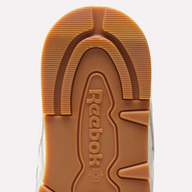 Close-up of the sole of the Reebok Men's Classic Leather Shoes, featuring the Reebok logo and a brown tread pattern with textured grooves, supported by an EVA midsole, displayed against a white background.