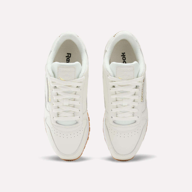 A pair of Men's Classic Leather Shoes by Reebok in white, shown from above with visible laces, perforated toe areas, and the Reebok logo on the sides and inside the shoes. Set against a plain white background, these sneakers also include an EVA midsole for lightweight cushioning.