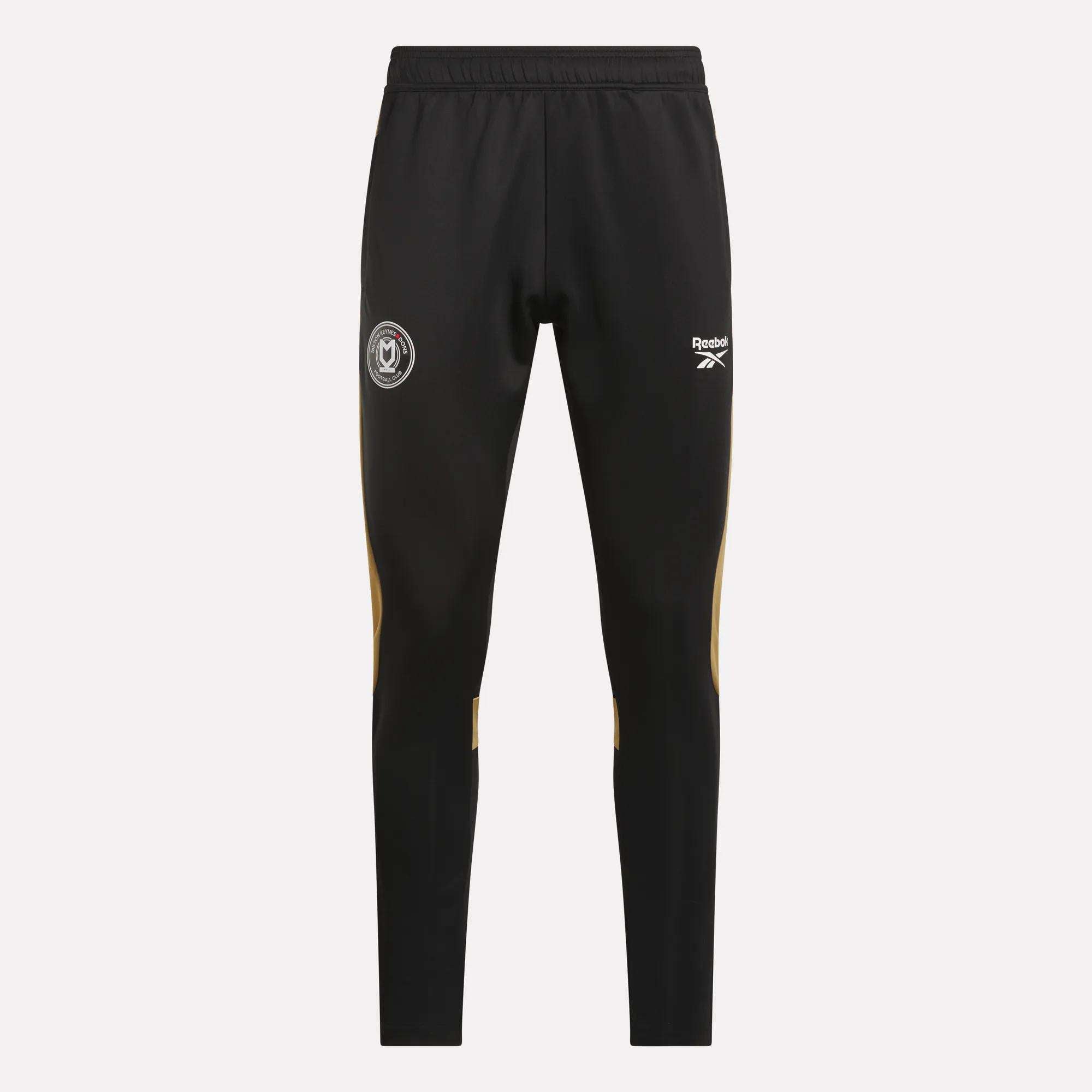 Reebok Men's MK Dons Travel Pants feature an elastic waistband, white logo and crest on the thighs, and yellow accents below the knees—ideal men's travel pants for dedicated football fans.