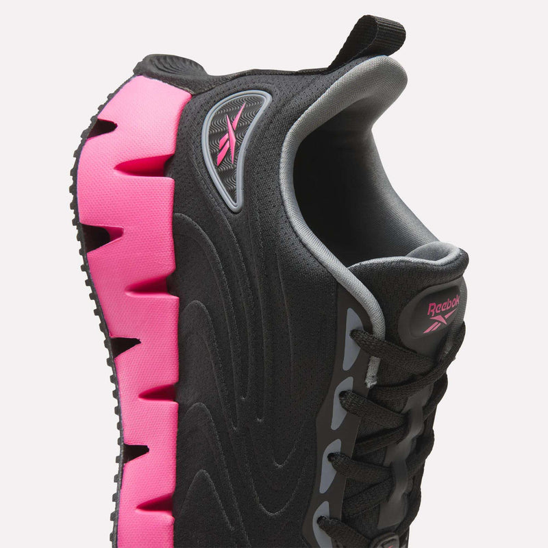Close-up of a Reebok Women’s Zig Futaura 1.0 shoe featuring a black mesh upper and a bright pink, zigzag-shaped FuelFoam midsole.