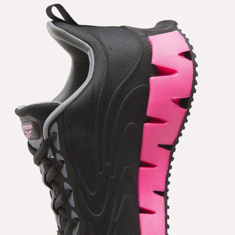 Close-up of a Women’s Zig Futaura 1.0 shoe with a black mesh upper and a bright pink, jagged-edge FuelFoam midsole.