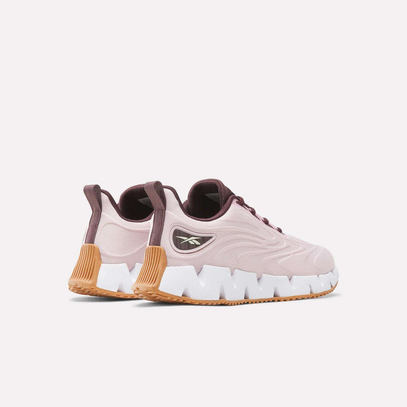 Women’s Zig Futaura 1.0 Shoes by Reebok in pale pink with dark purple accents, a thick white zig-zag FuelFoam midsole, and a tan rubber outsole.