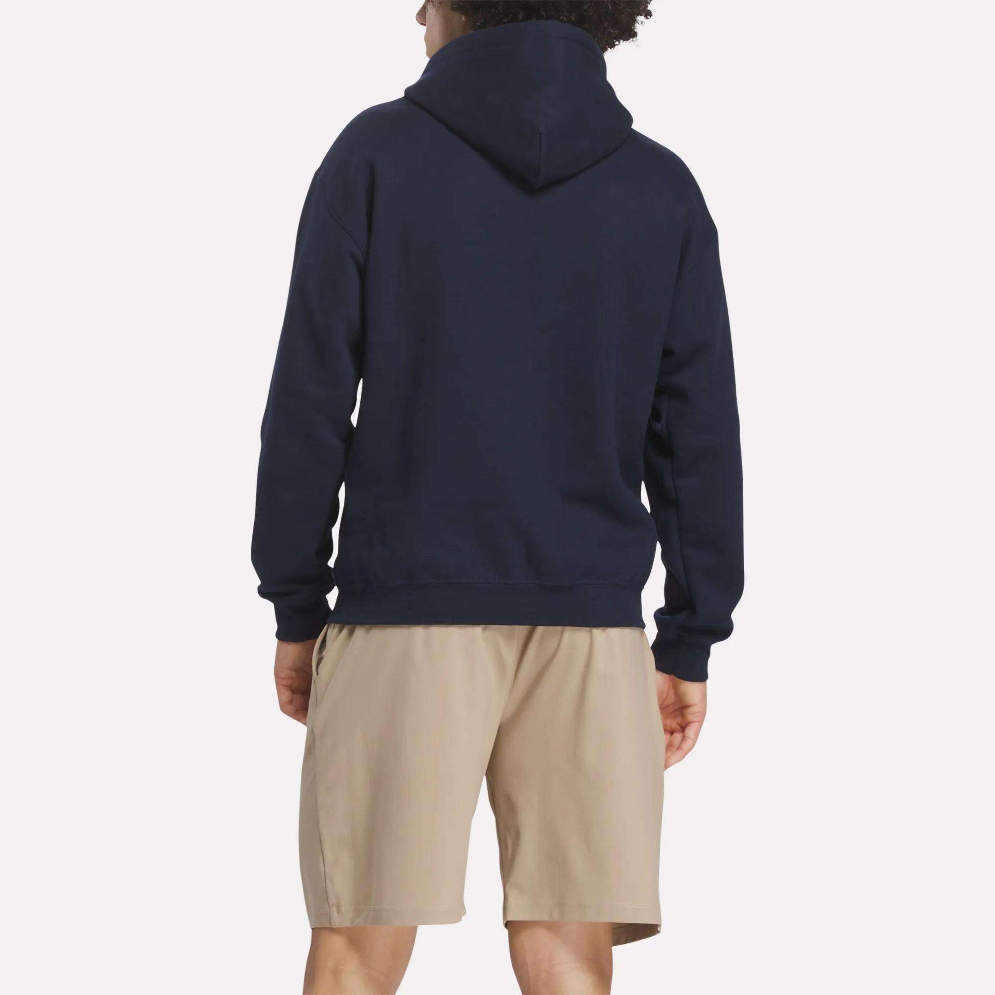 A person stands facing away from the camera, wearing a navy blue Reebok Men's Crushers Hoodie and light beige shorts against a plain white background.