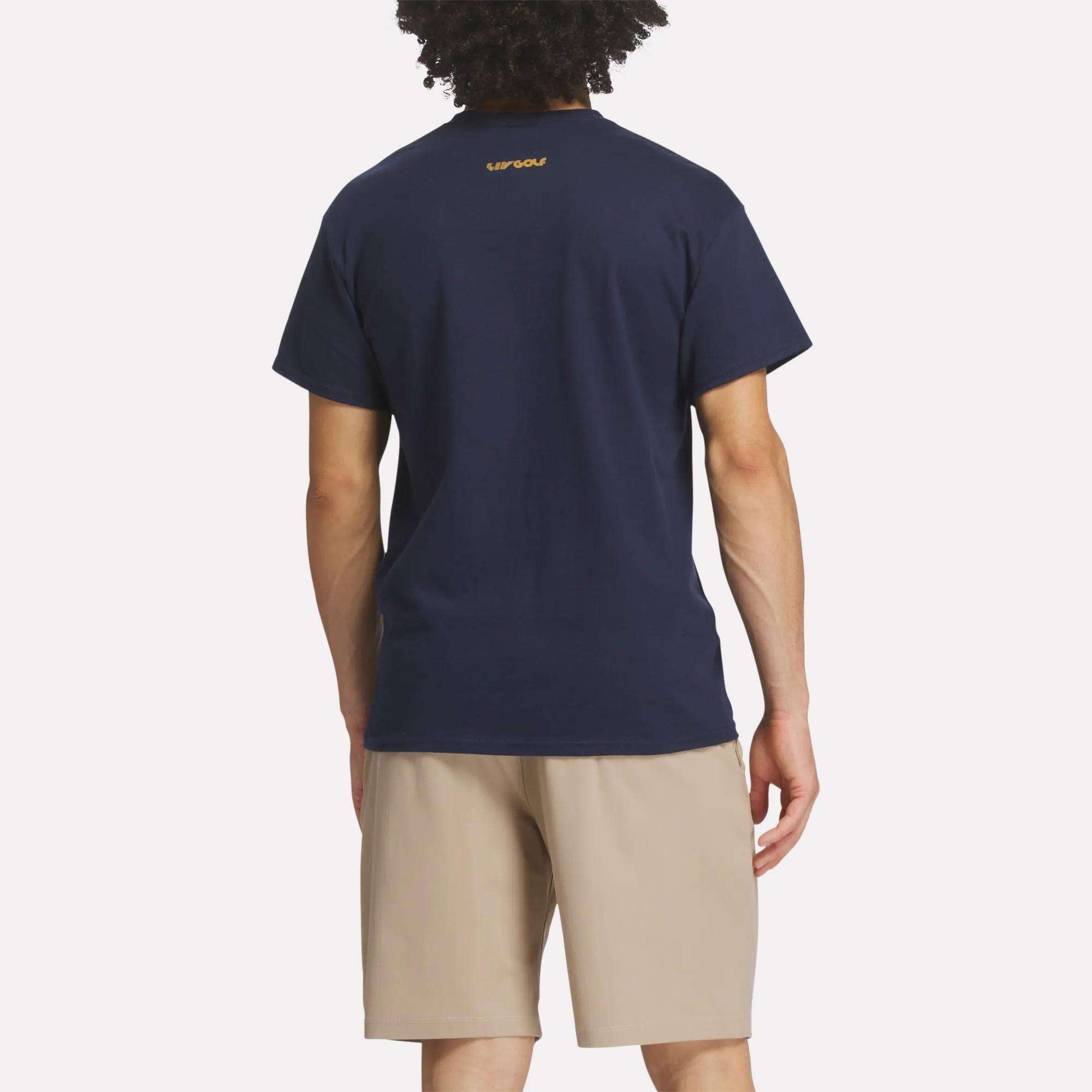 A person with curly hair is seen from behind, wearing the Reebok Men's Crushers Stacked Logo Tee in navy blue with a small yellow logo near the collar and light beige shorts, standing against a plain white background.