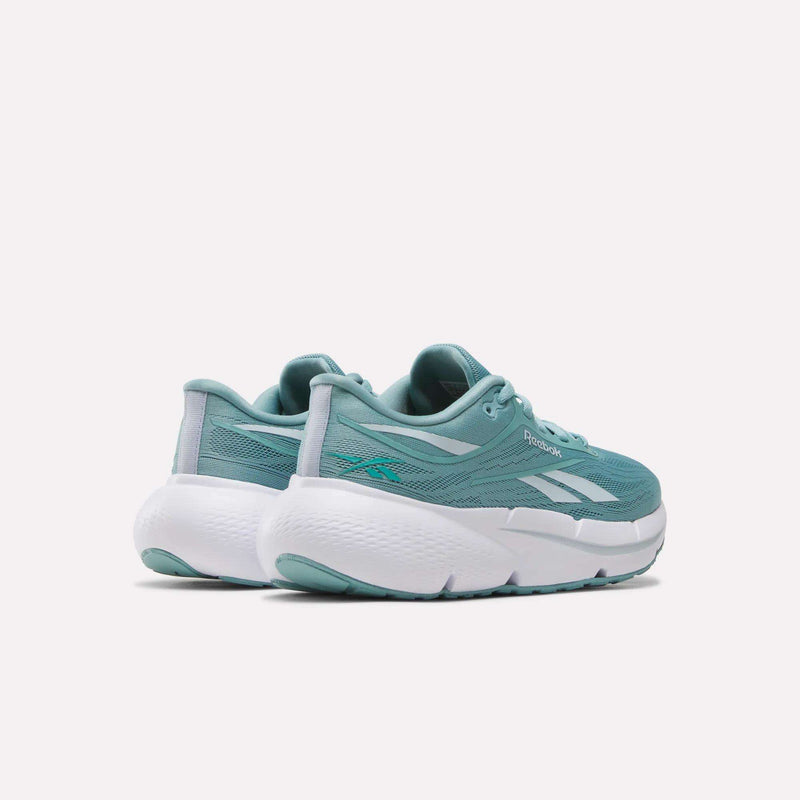 A pair of Reebok Women’s Zignition Running Shoes in teal, featuring white thick soles, are shown from the back and side against a plain white background. These athletic shoes offer springy cushioning for enhanced comfort and support.