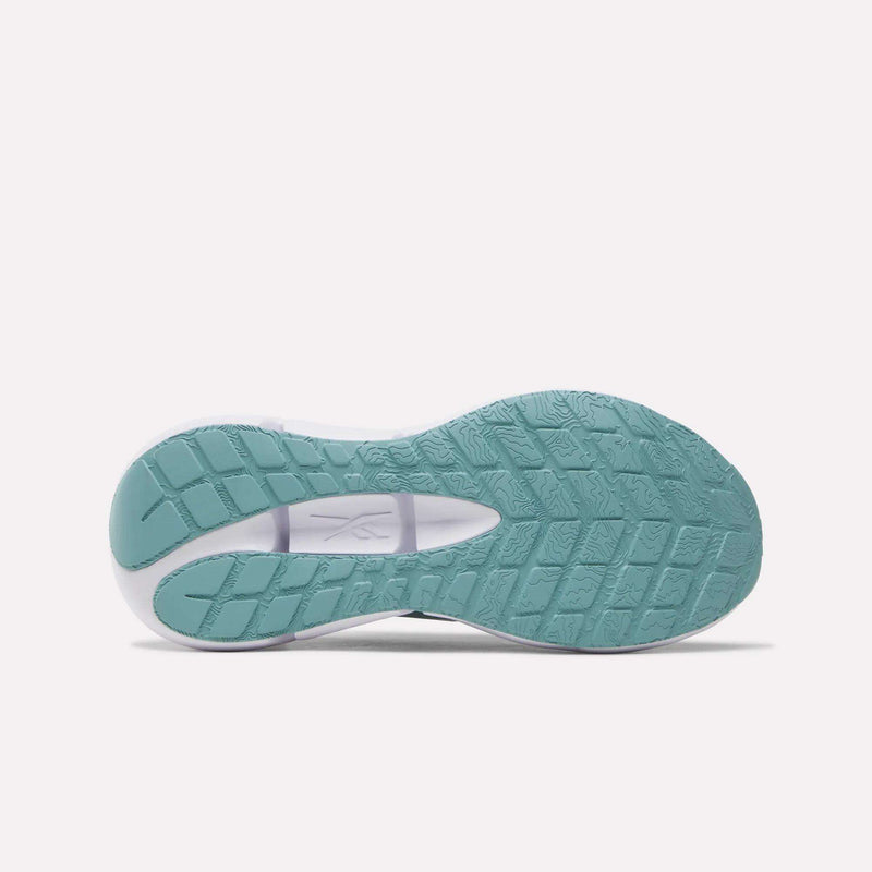 The image displays the teal rubber outsole of the Reebok Women’s Zignition Running Shoes, viewed from beneath, highlighting textured grip patterns and a contrasting white midfoot section. The design features rocker geometry to promote smooth transitions and responsive cushioning that delivers enhanced comfort with every step.