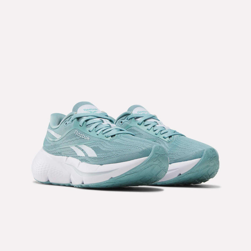 A pair of Reebok Women’s Zignition Running Shoes in teal, featuring white soles and white logo accents, with springy cushioning for enhanced comfort, displayed on a plain white background.