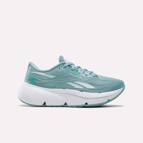 The Reebok Women’s Zignition Running Shoes in Tranquil Teal/White are shown from the side on a white background, featuring a light teal mesh upper with white accents and the Reebok logo, plus a thick, cushioned white sole for springy comfort.