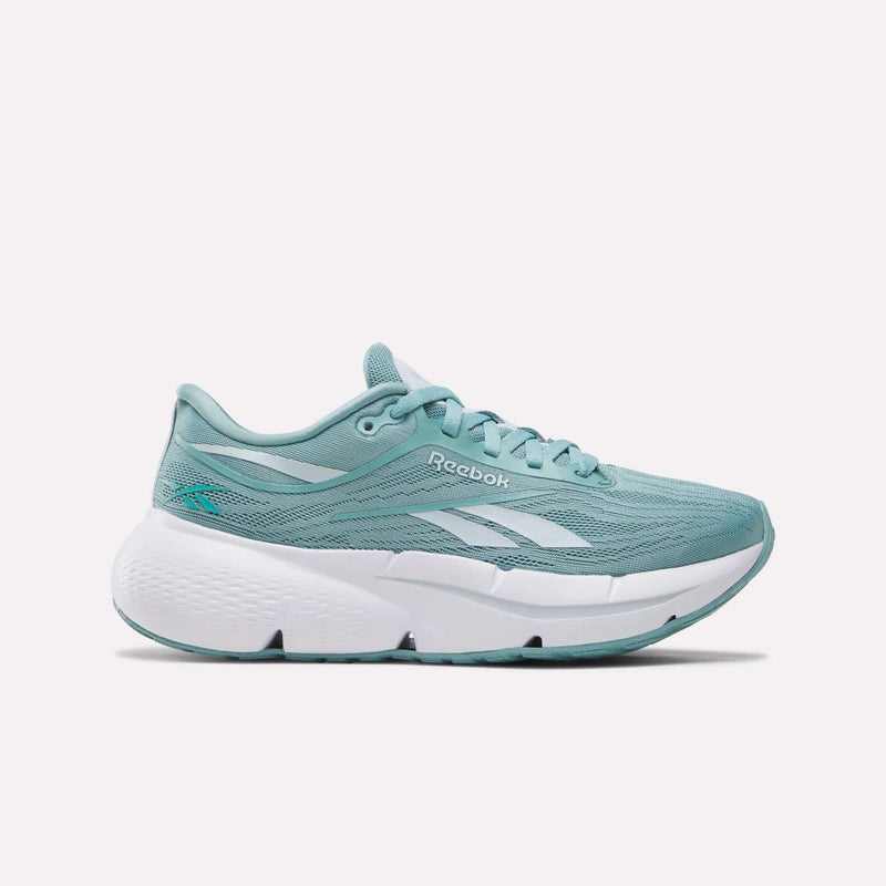 The Reebok Women’s Zignition Running Shoes in Tranquil Teal/White are shown from the side on a white background, featuring a light teal mesh upper with white accents and the Reebok logo, plus a thick, cushioned white sole for springy comfort.