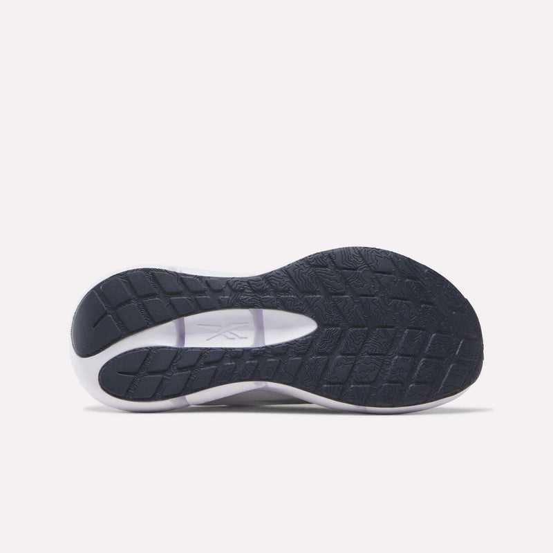 The image displays the bottom view of a black and white Reebok Women’s Zignition Running Shoe sole, featuring textured grip patterns and the Reebok logo in the center, designed with springy cushioning to enhance comfort and performance for runners.