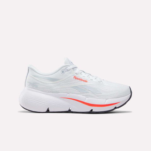 The Reebok Women’s Zignition Running Shoes in White/Neon Cherry feature a thick sole with springy cushioning and rocker geometry for smooth, effortless motion. These white running shoes have light gray accents, an orange (neon cherry) Reebok logo, an orange stripe along the sole, and a textured heel. Displayed on a plain white background.