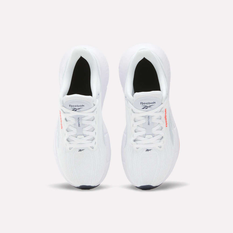 Top-down view of a pair of Reebok Women’s Zignition Running Shoes in white, featuring black soles, light gray laces, and the Reebok logo on the tongue and side, placed side by side on a light background. Designed with springy cushioning, these shoes provide enhanced comfort and support during every stride.