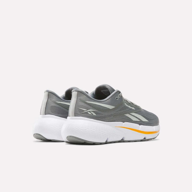A pair of Reebok Men’s Zignition Running Shoes in gray, featuring white soles and yellow accents, springy cushioning, and a wider forefoot, displayed on a light background and angled to showcase the back and sides.