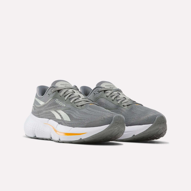 A pair of Reebok Men’s Zignition Running Shoes in gray with white and yellow accents, featuring white cushioned soles, responsive springy cushioning for enhanced comfort, and breathable mesh uppers, displayed on a plain white background.