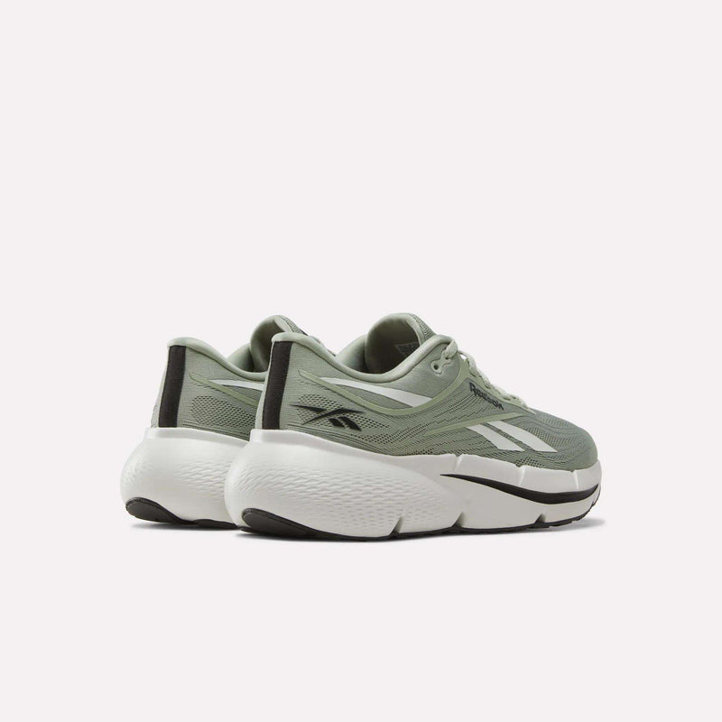 A pair of Reebok Men’s Zignition Running Shoes in sage green and white, featuring thick white soles, black accents, and mesh uppers with a wide forefoot and springy cushioning, shown from the back and side against a plain light background.