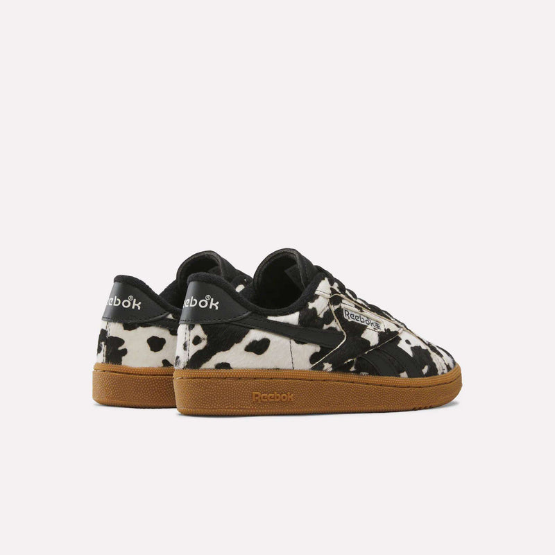 A pair of Reebok Women’s Club C Grounds UK 1.0 Shoes featuring a black and white cow print pattern and brown gum soles, displayed against a plain light background.