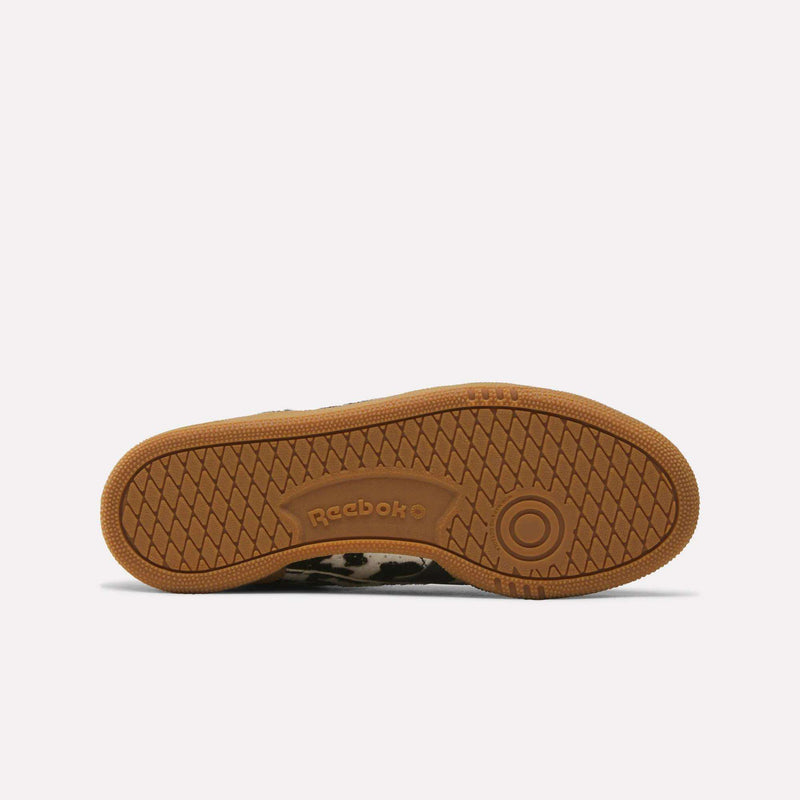 The image shows the brown rubber sole of the Reebok Women’s Club C Grounds UK 1.0 Shoes, featuring a herringbone tread pattern and the Reebok logo embossed near the center.