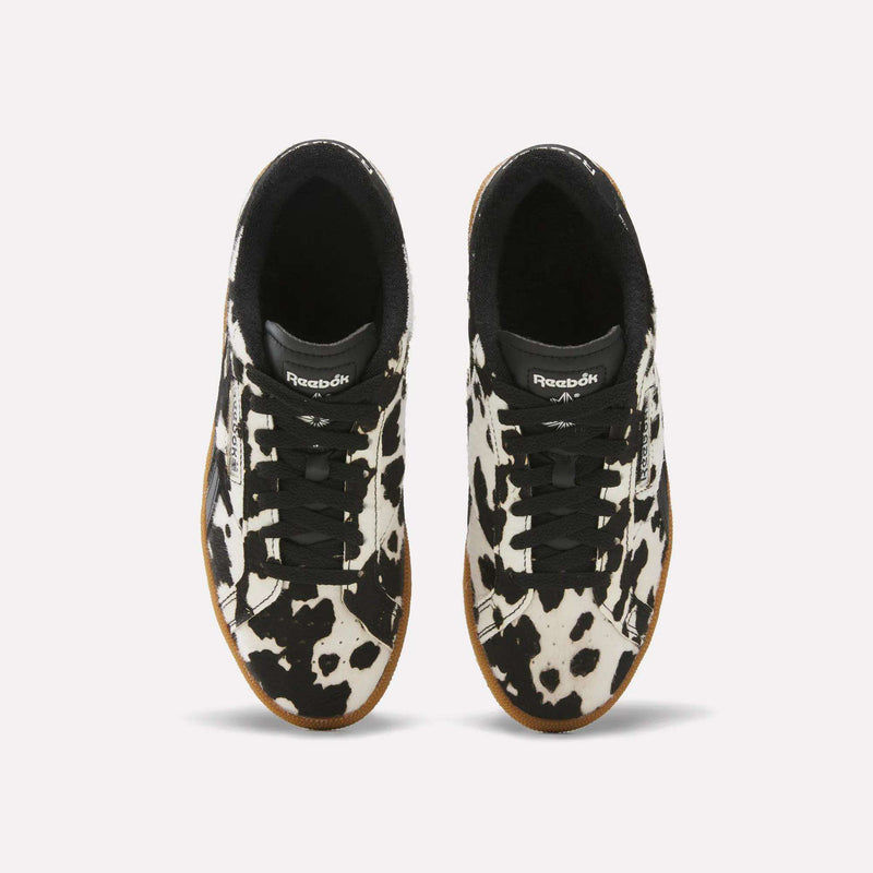 A pair of Women’s Club C Grounds UK 1.0 Shoes by Reebok, styled with black laces and a striking black and white cow print design, are displayed from an overhead perspective on a plain white background—ideal for those who love animal print sneakers combined with classic Reebok flair.