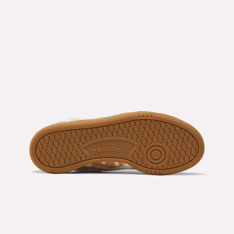 The image shows the brown rubber sole of the Women’s Club C Grounds UK 1.0 Shoes by Reebok, viewed from the bottom. The sole features a herringbone tread pattern and a circular detail near the toe. Combining classic style with a twist, this women’s sneaker includes subtle animal print accents and an embossed Reebok logo at the arch.