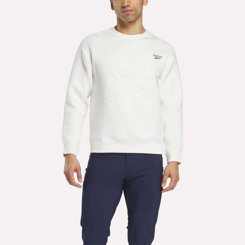 A man in a white Reebok Men's Scuba Knit Crew Sweatshirt with an embossed front design and navy pants stands against a plain white background.