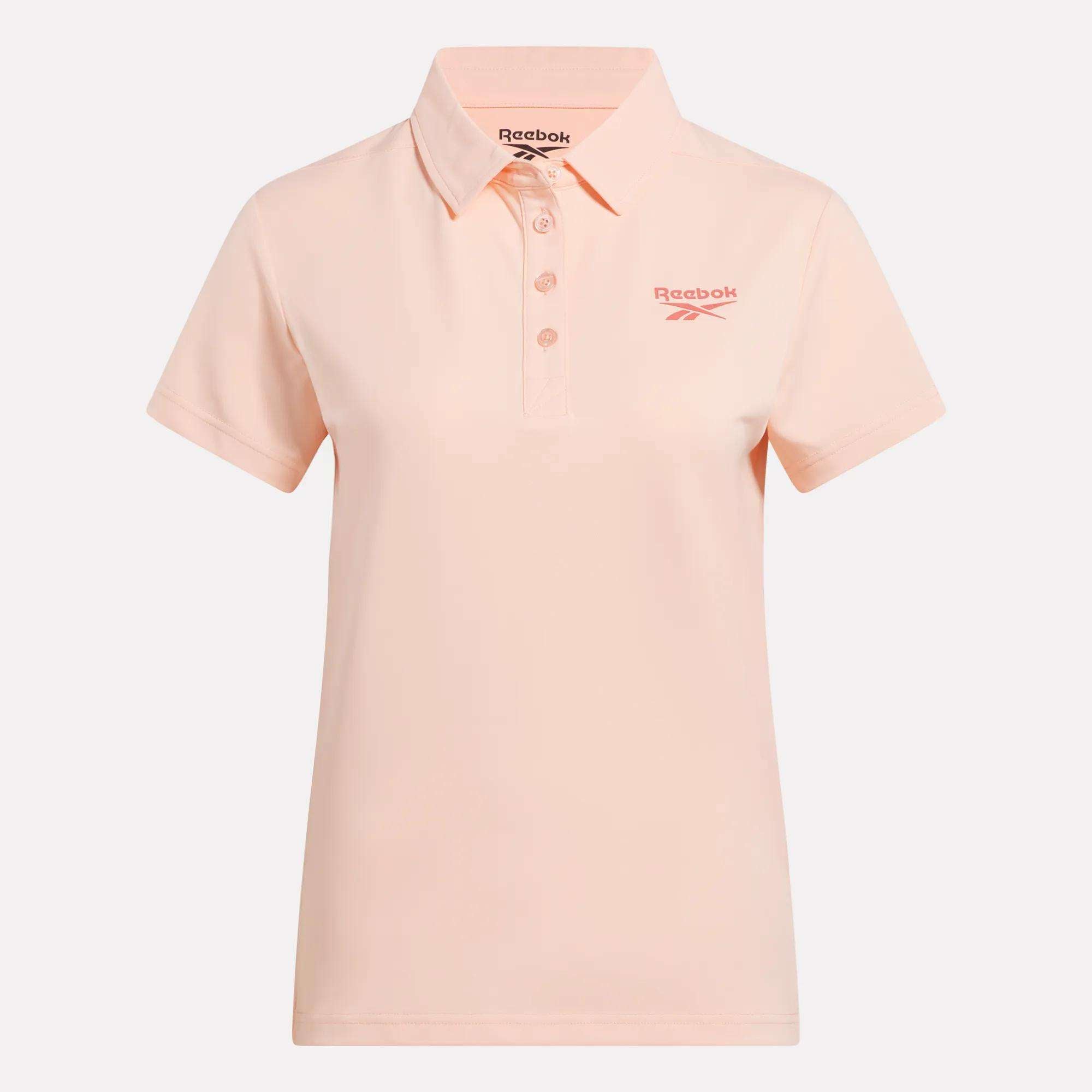 The Reebok Women's Micro Pique Polo Shirt is light pink with stretch fabric, short sleeves, a collar, button placket, and a pink Reebok logo on the left chest. It is displayed against a plain white background.