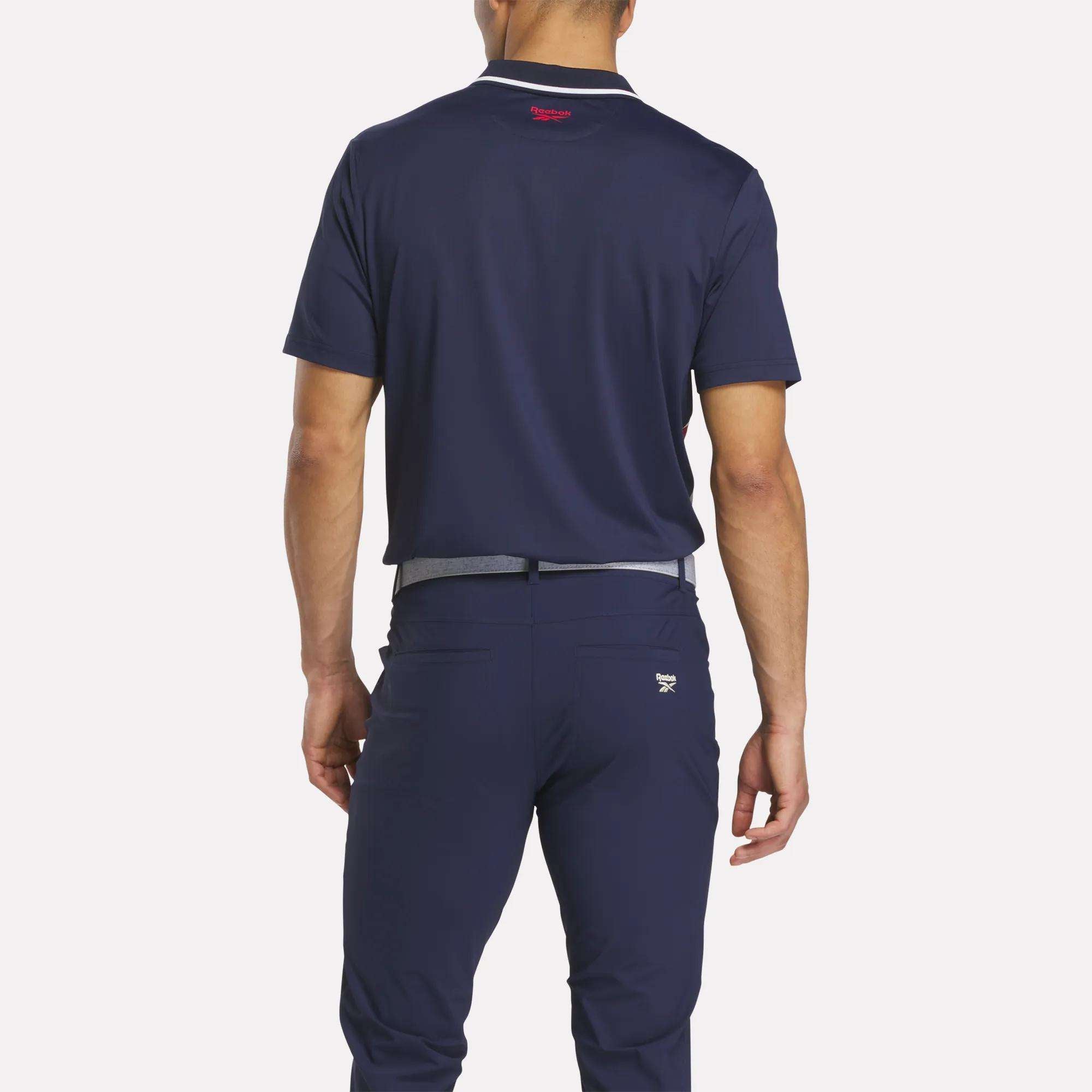 A man stands with his back to the camera, wearing a Reebok Men's Vector Argyle Print Polo in navy and matching navy pants with a light gray belt, both crafted from stretch knit fabric for superior comfort.