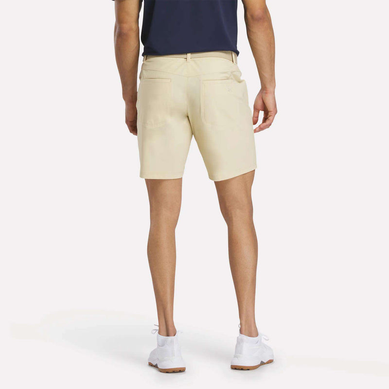 A person wearing a navy blue shirt, Reebok Men's Favorite Golf Shorts 8.5", and white sneakers stands with their back to the camera against a plain white background.