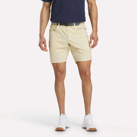 A man in a navy shirt, black belt, white sneakers, and Reebok Men's Favorite Golf Shorts 8.5" stands against a plain white background. His face is not visible.