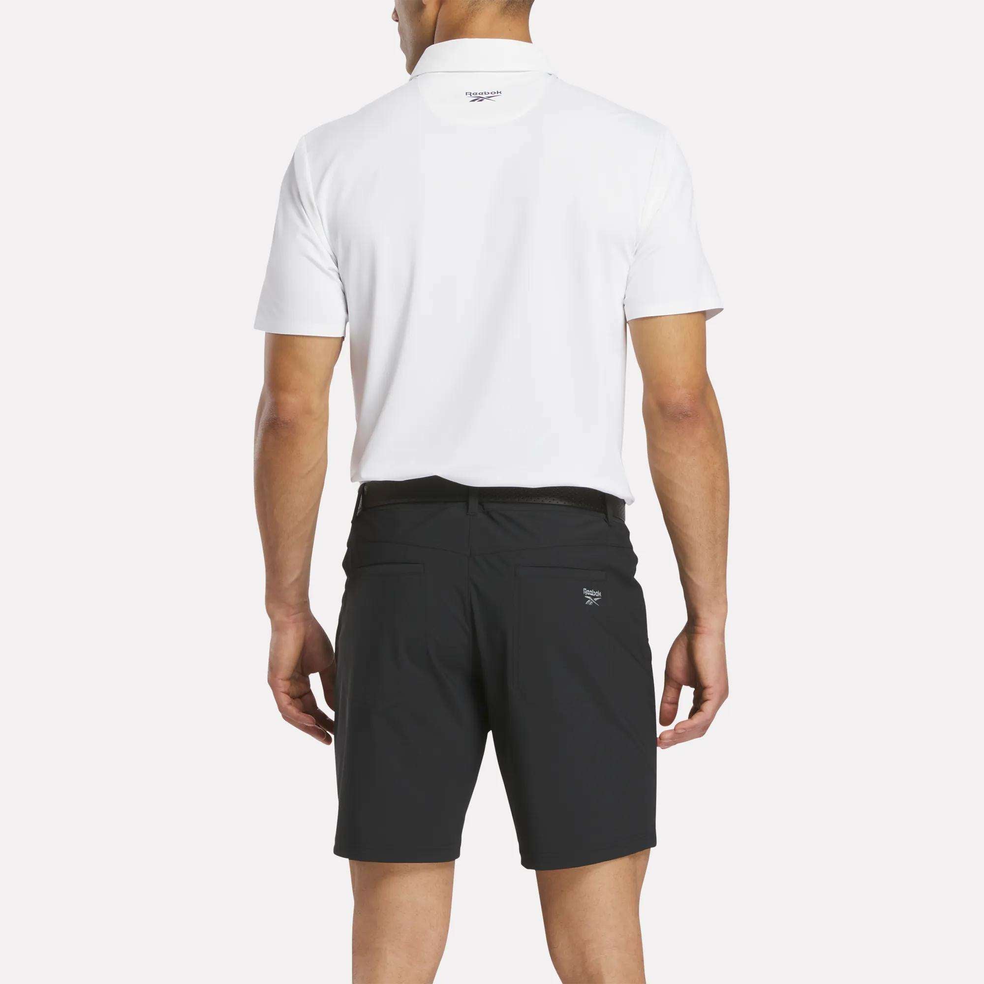 A man faces away from the camera, wearing a white polo and Reebok Men's Favorite Golf Shorts 8.5" in black, set against a plain white background.
