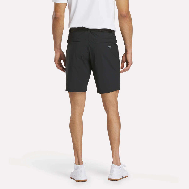 A person wearing a white shirt, Reebok Men's Favorite Golf Shorts 8.5", and white sneakers stands facing away from the camera against a plain light background.