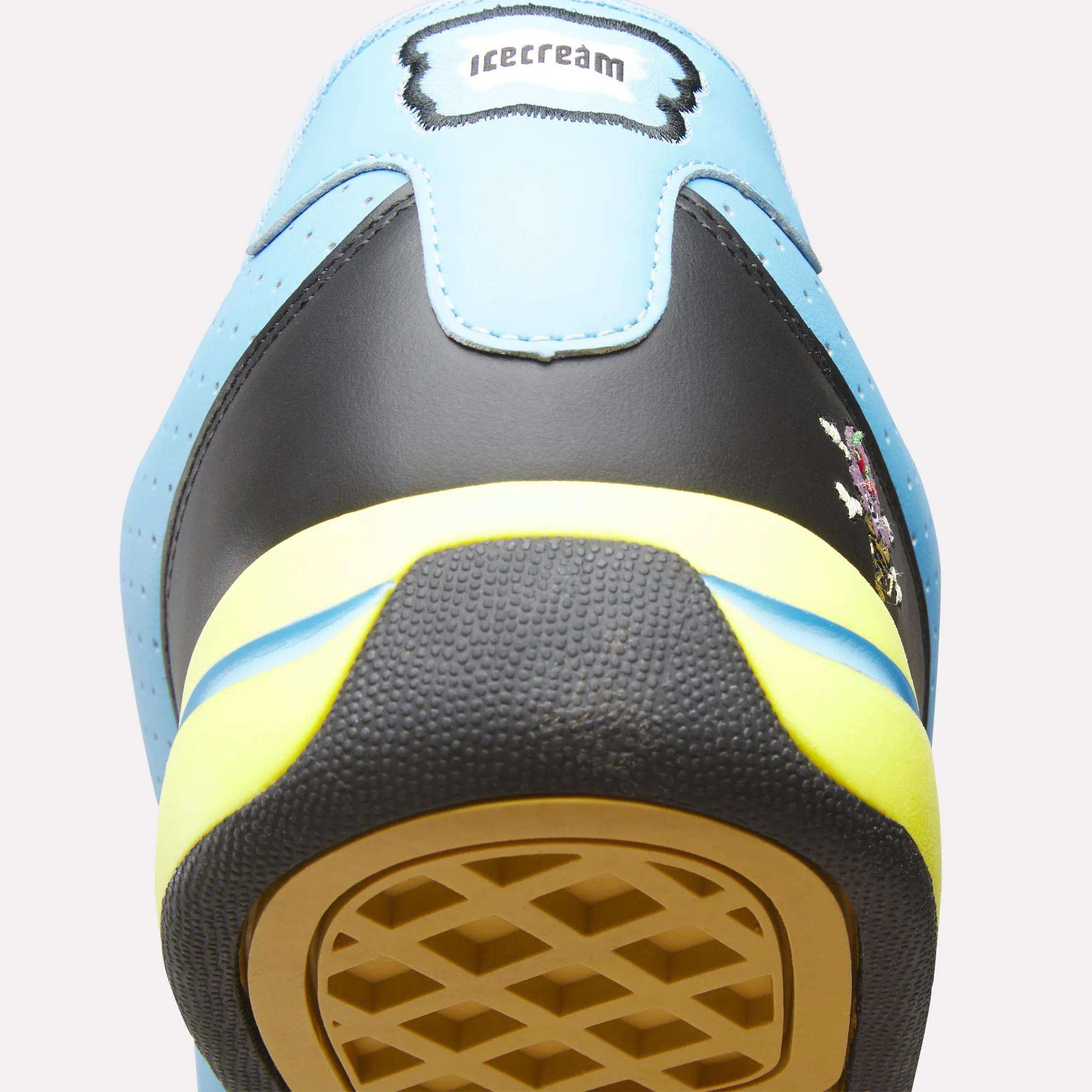 Close-up of the heel of a Reebok x Icecream Board Flip Shoe in light blue, black, and yellow. A label at the top reads "icecream," and the sole features a unique waffle-like pattern. Brand: Reebok.