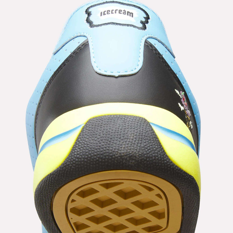 Close-up of the heel of a Reebok x Icecream Board Flip Shoe in light blue, black, and yellow. A label at the top reads "icecream," and the sole features a unique waffle-like pattern. Brand: Reebok.