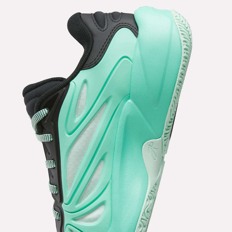 A close-up of the Reebok Angel Reese 1 Basketball Shoes for Big Kids, featuring a teal sole and side details, a white midsection, and black upper accents, displayed against a white background.