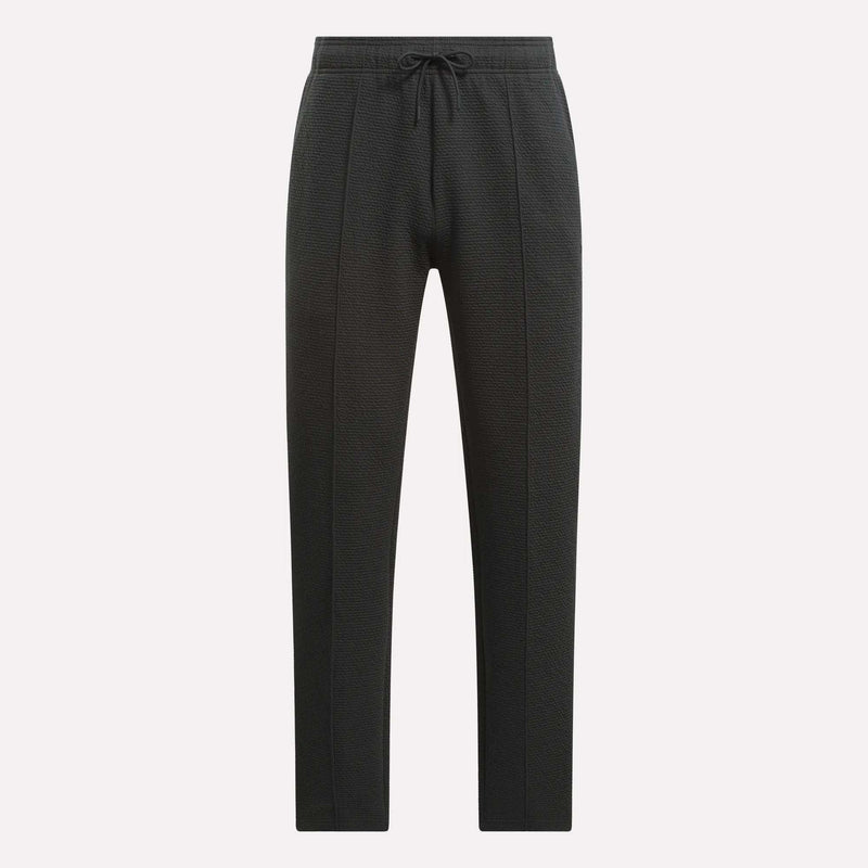 Men's Club Sport Textured Pants by Reebok feature a black textured design, slim tapered fit, and drawstring waistband with front panel seams and tapered legs, shown against a plain white background.