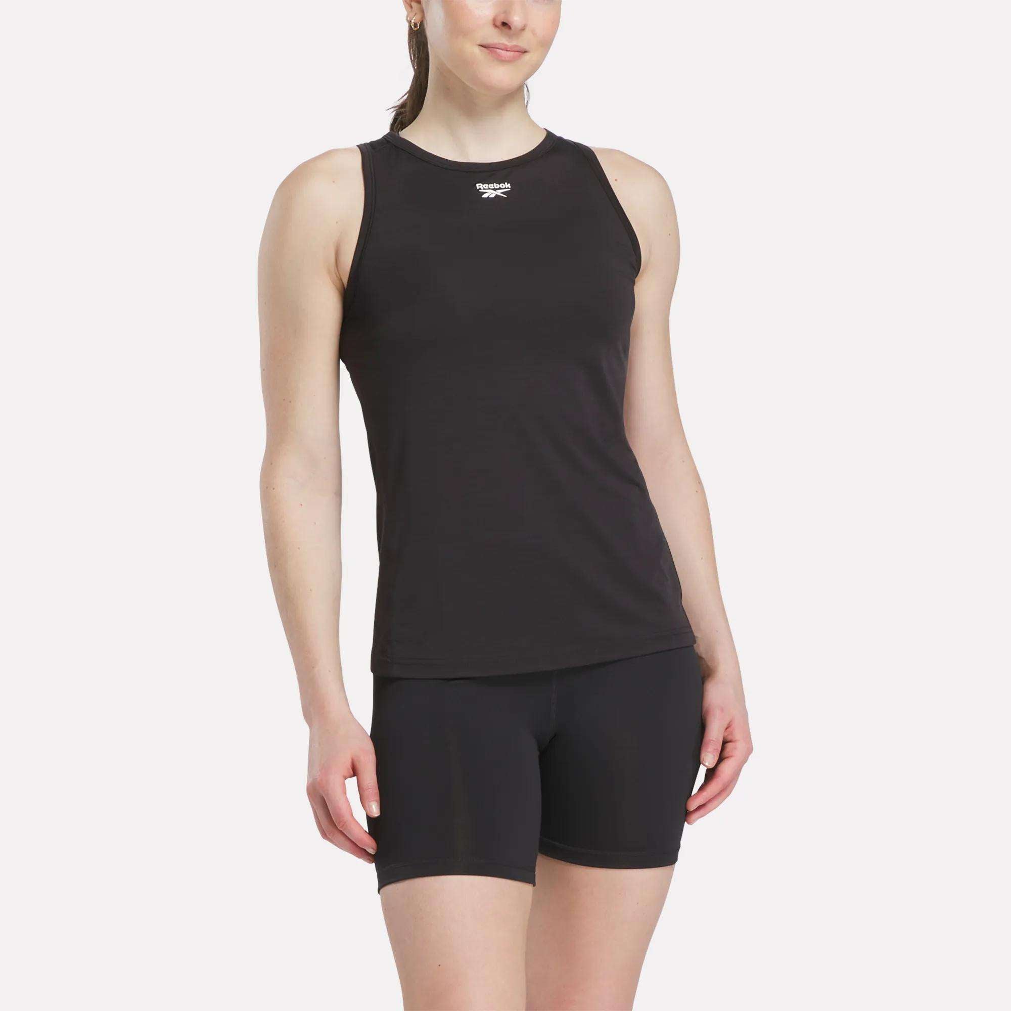 A woman wearing the Reebok Women's Marled Performance Tank Top stands with one arm relaxed by her side, smiling slightly against a plain white background.