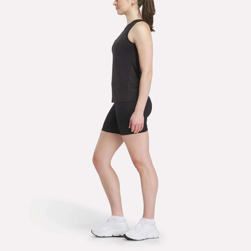 A woman in profile faces left, wearing a Reebok Women's Marled Performance Tank Top and black shorts with white athletic shoes—ideal activewear—set against a plain white background.