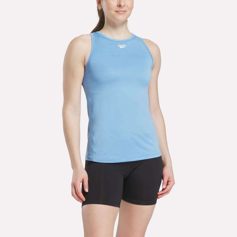 A woman wears a Reebok Women's Marled Performance Tank Top in light blue with black shorts, standing against a plain white background.