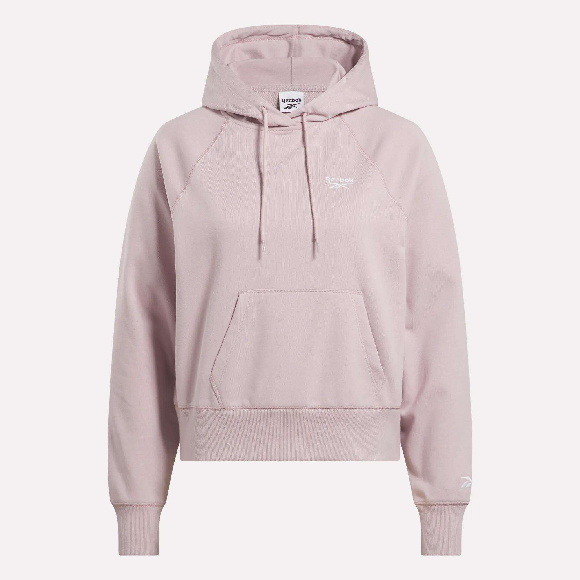 The Women's Small Vector Cropped Hoodie by Reebok comes in light pink French terry, featuring a front pocket, drawstrings, and white logos on the chest and sleeve. Shown against a plain white background.