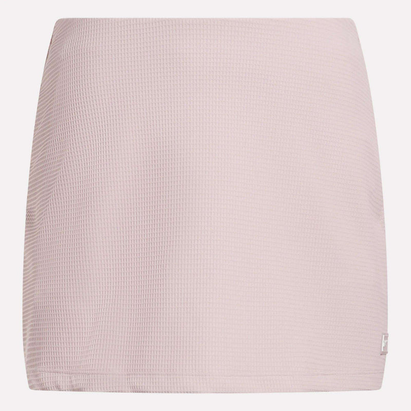 The Reebok Women's Time Out Slim Tennis Skort features a light pink, waffle-textured fabric and straight cut—a minimal design ideal for sporty flair in your activewear wardrobe. Shown against a white background.