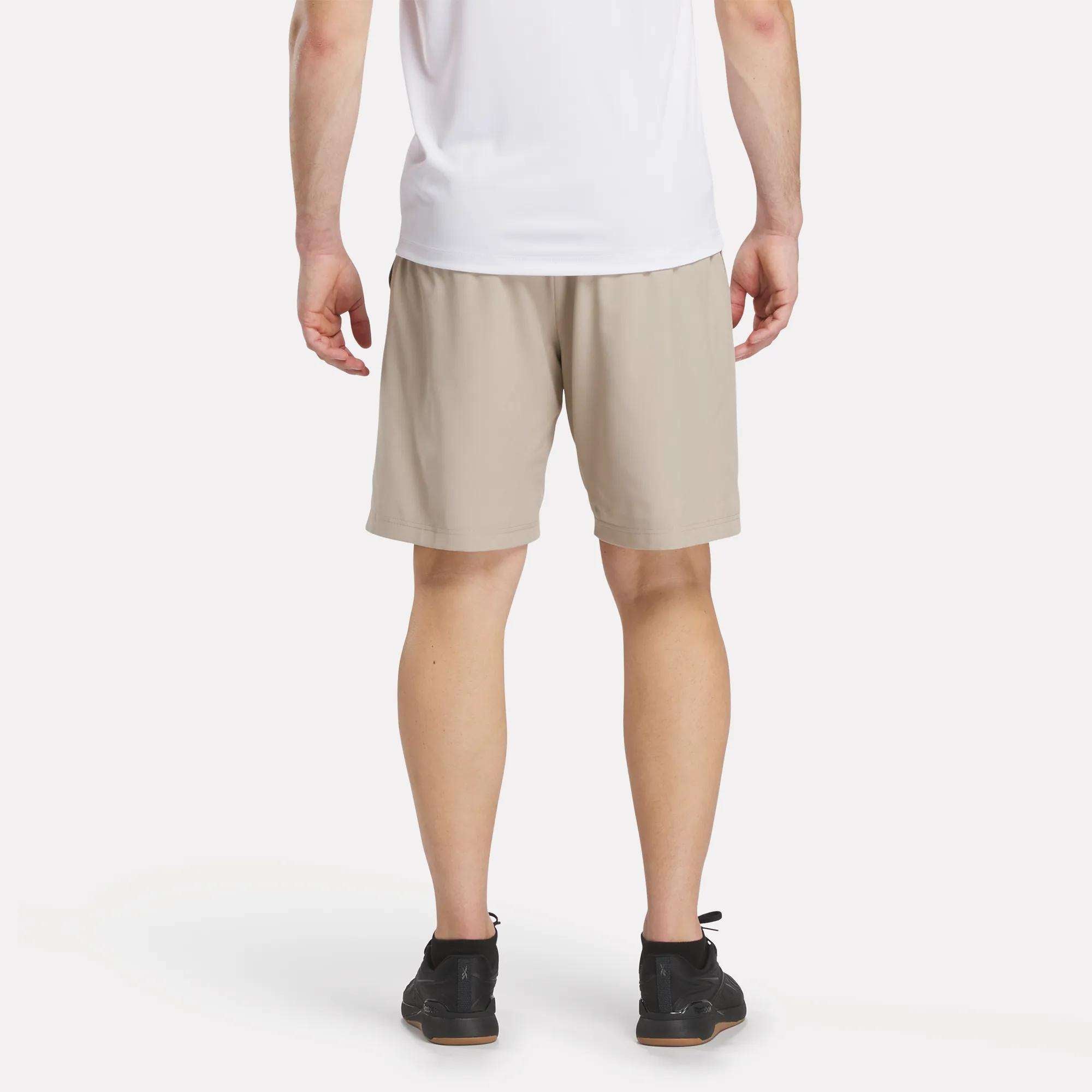A person in a white t-shirt and Reebok Men's Range Shorts 9" with black sneakers stands with their back to the camera against a plain white background.